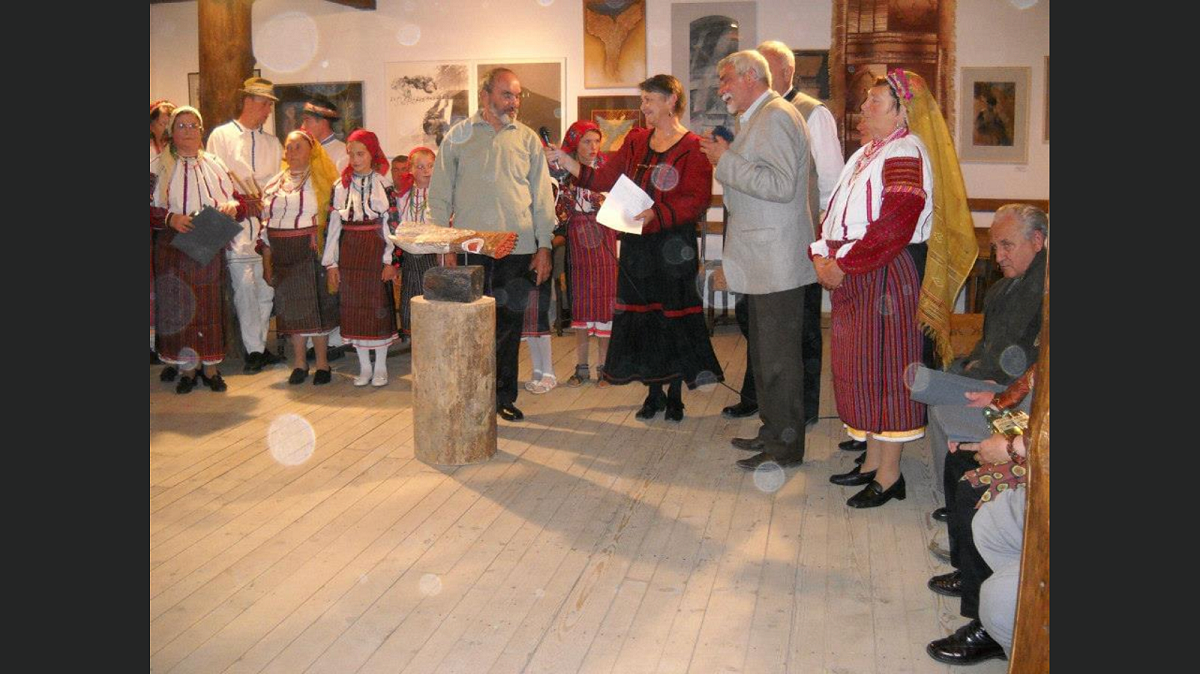 Guests and performers in traditional folk costume gathered at an art exhibition in the Gyimesi Skanzen heritage village.