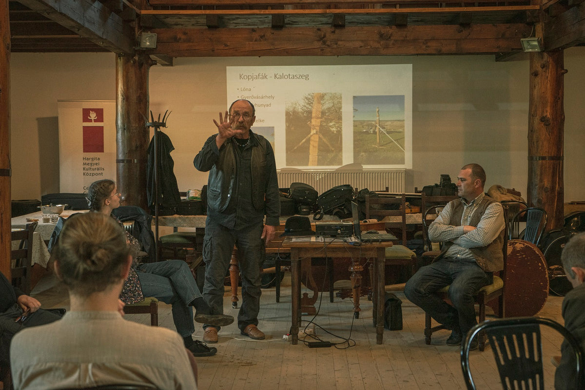 Speaker giving a presentation on traditional carved wooden memorial posts to folk musicians.