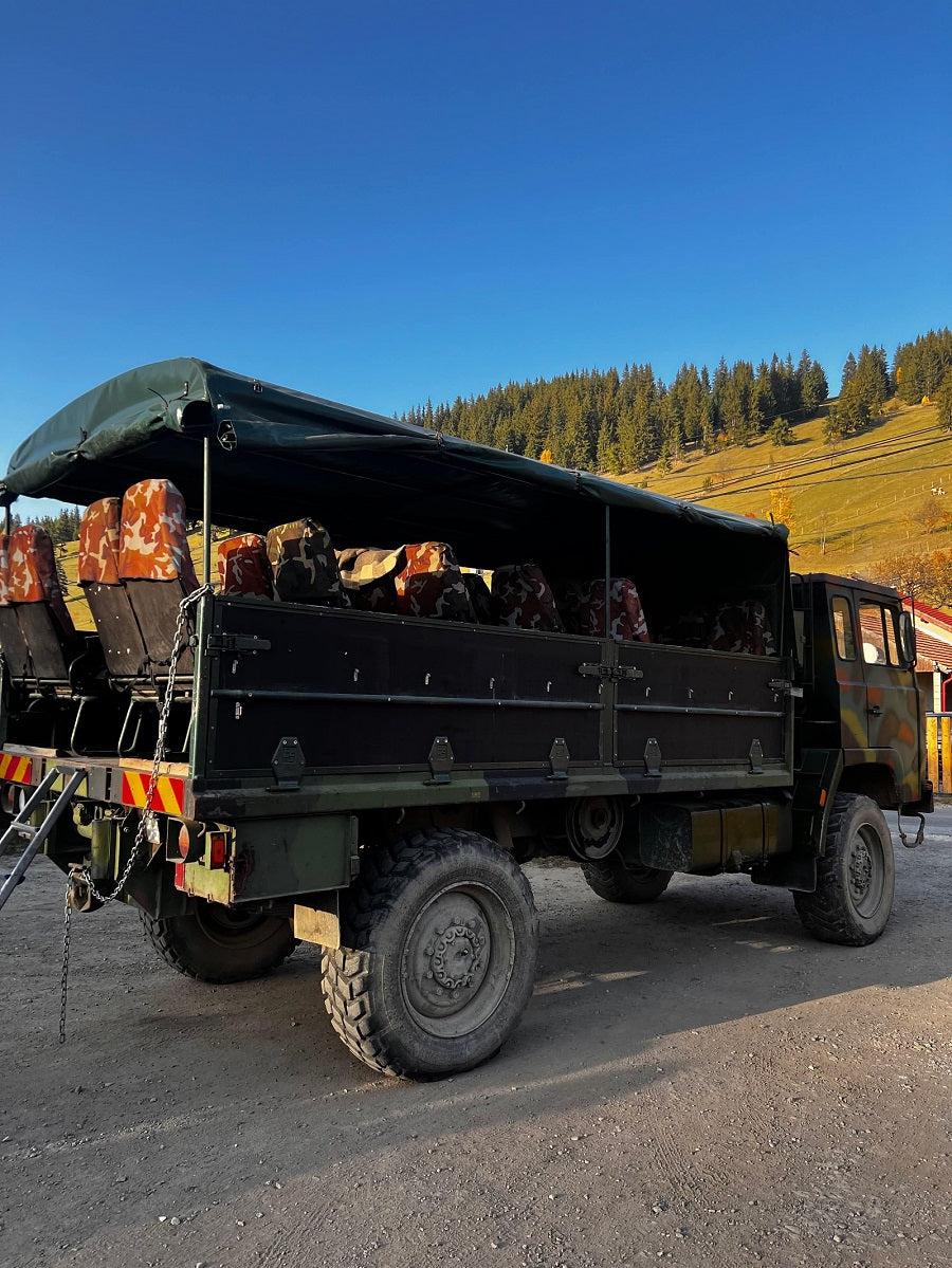 An open-bed off-road tour truck with camouflage-patterned seats, parked before autumn hillsides.