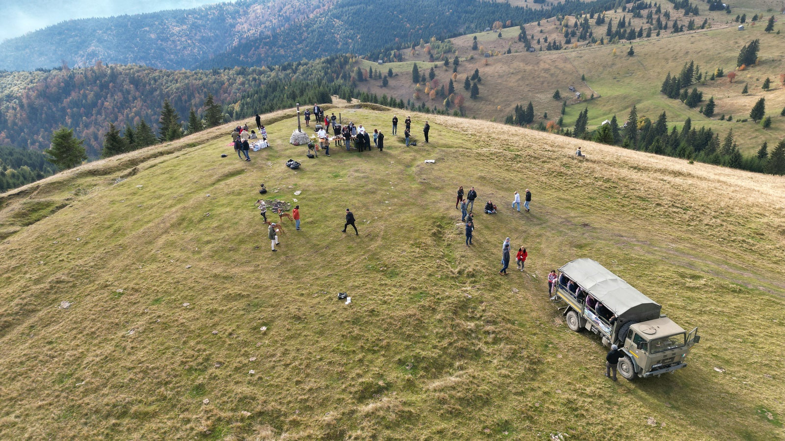 Aerial view of a group gathered on a mountain summit beside the off-road tour truck.