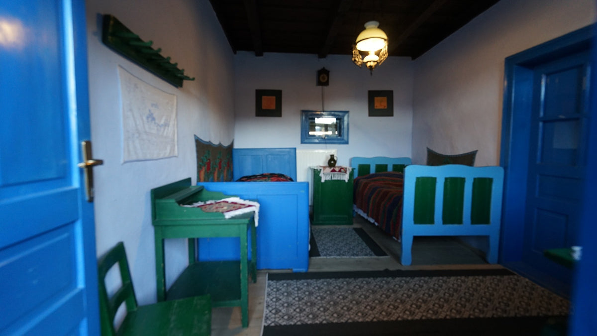 Bedroom with bright blue and green painted furniture, a striped bedspread, and folk-embroidered wall hangings.