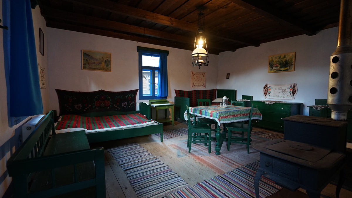 Room with a green painted bed and dining set, a floral tapestry headboard, and a wood-burning cook stove.
