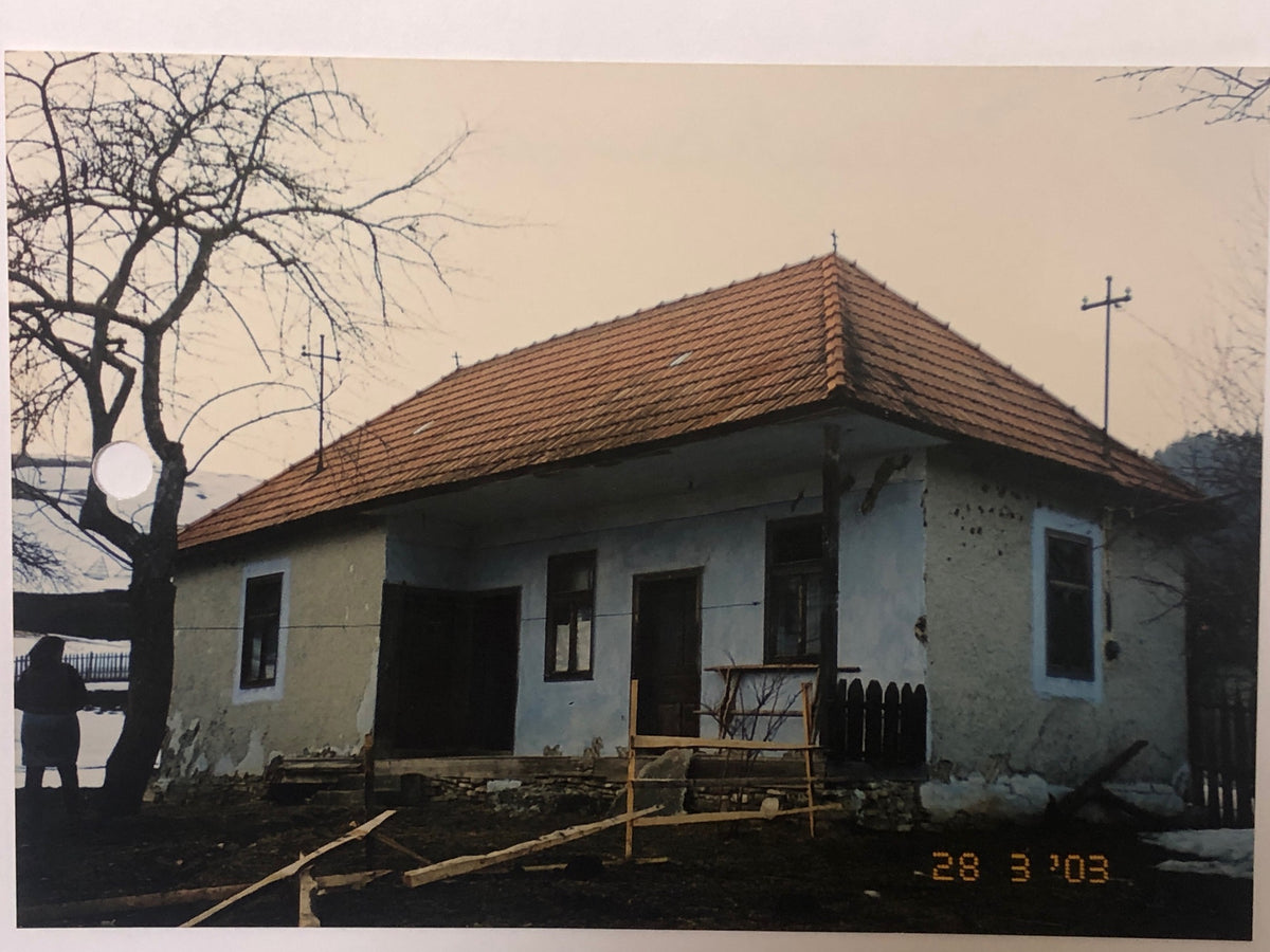 Archival photo of the Bálványos house mid-restoration in March 2003, with bare trees and scattered building materials.