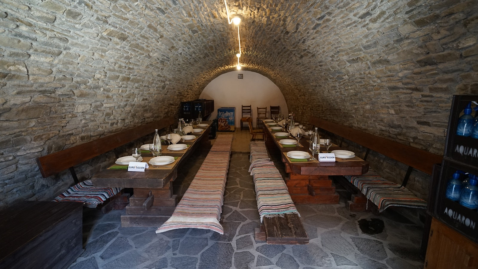 Wine cellar set for a dinner event, with two long tables laid with plates, wine glasses, and place cards.
