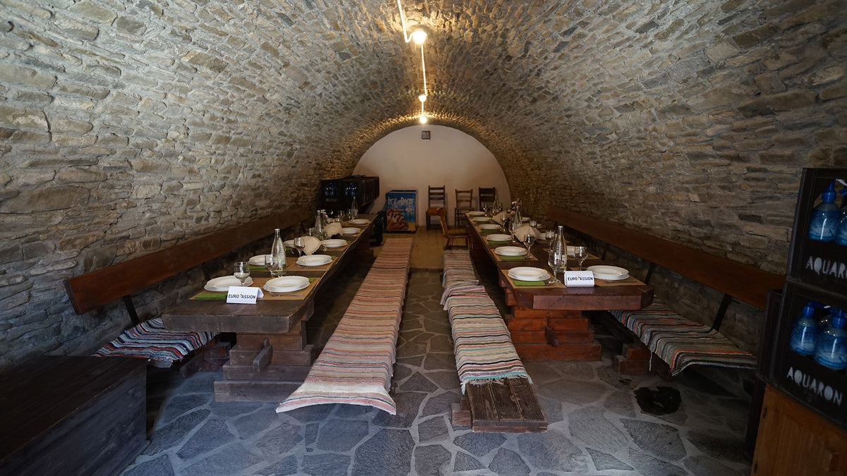 Wine cellar set for a dinner event, with two long tables laid with plates, wine glasses, and place cards.