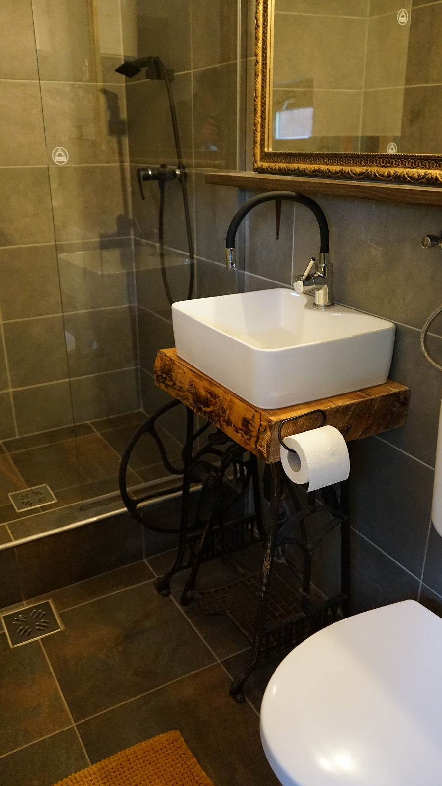 Bathroom with a vessel sink on a repurposed antique sewing-machine stand, beside a glass-walled shower.