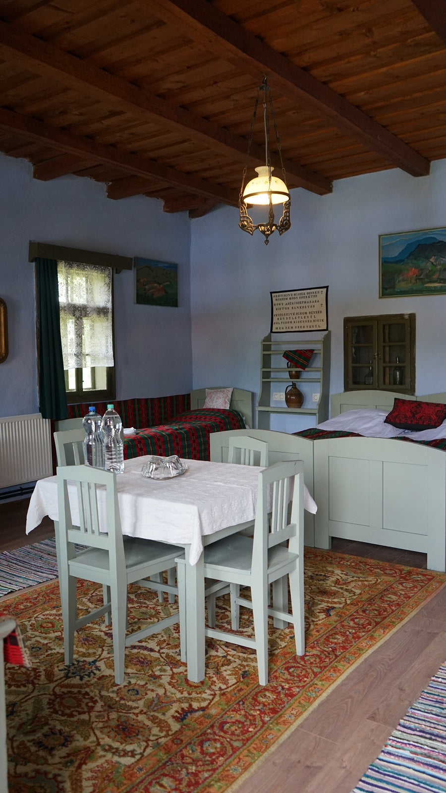 Pale blue bedroom with pastel green furniture, red and green folk-pattern bedding, and a patterned rug.