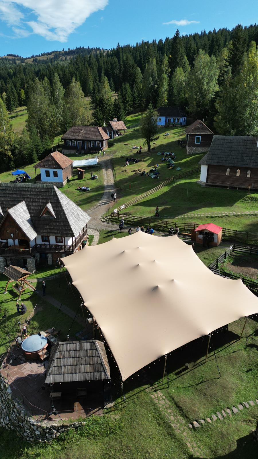 Aerial view of traditional village houses and event tent surrounded by forested hills at Gyimesi Skanzen.