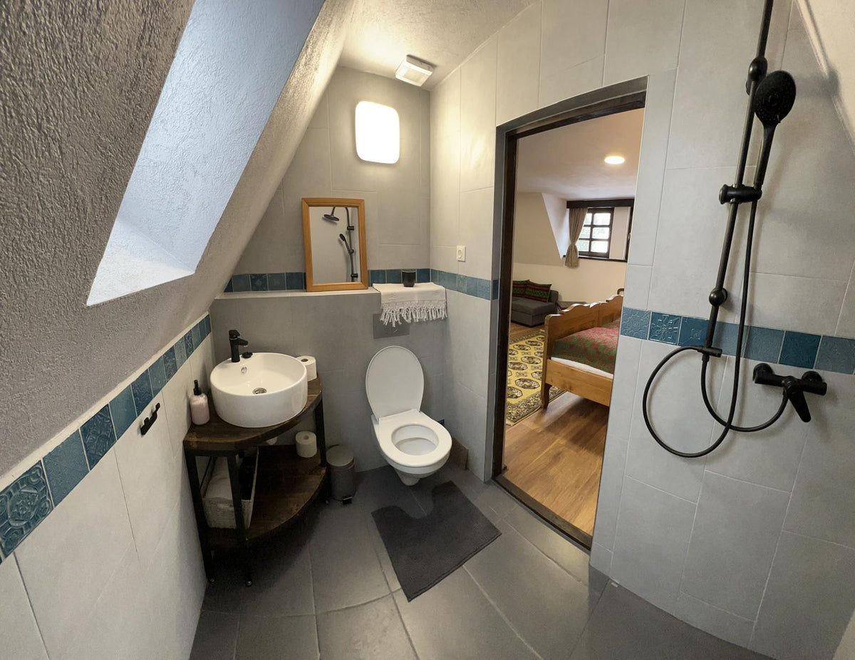 Attic bathroom with black shower fixtures and a corner vessel sink, doorway open to a bedroom.