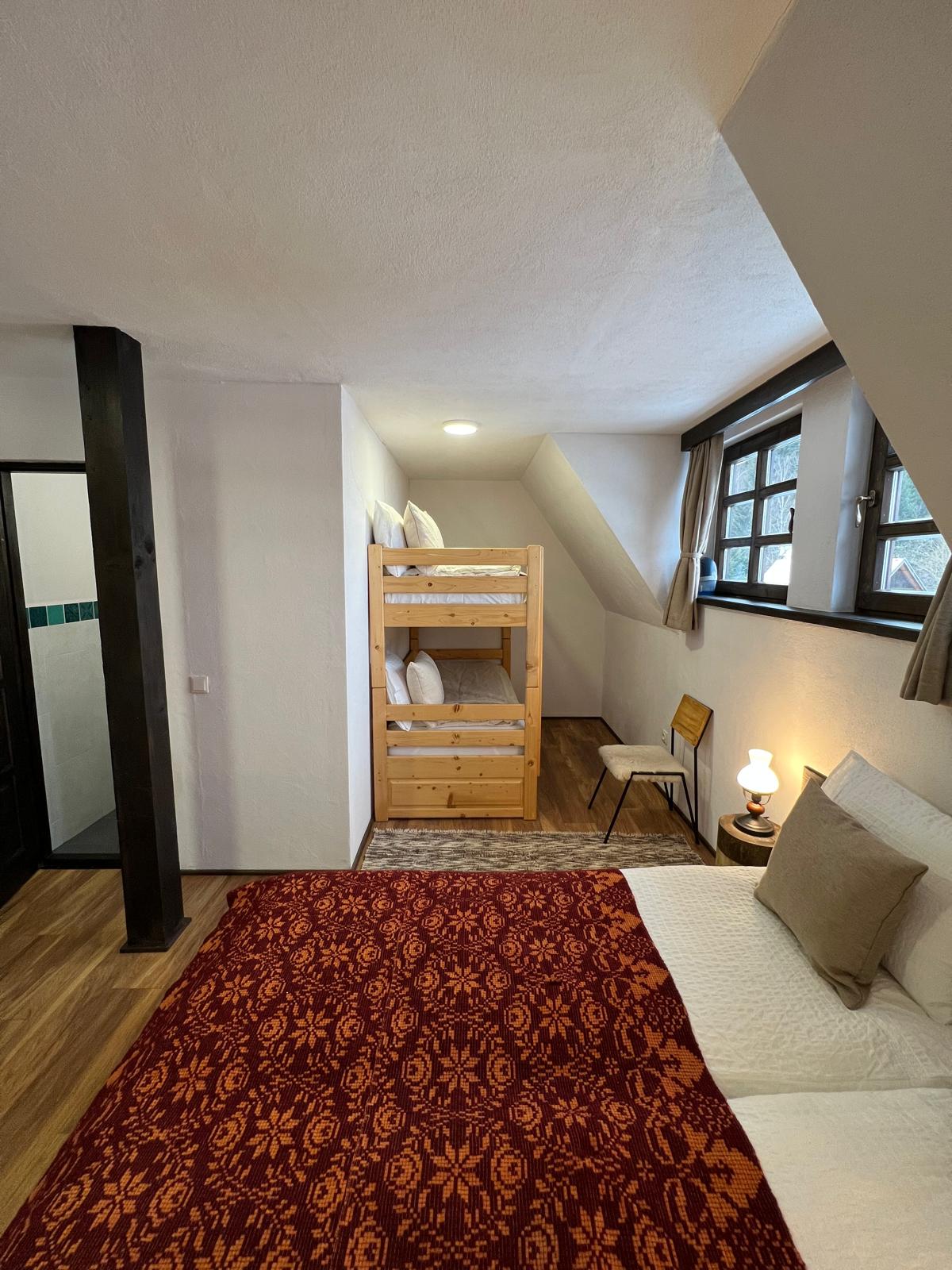 Attic bedroom with a double bed in a red and orange folk-pattern throw, beside a plain wood bunk bed.