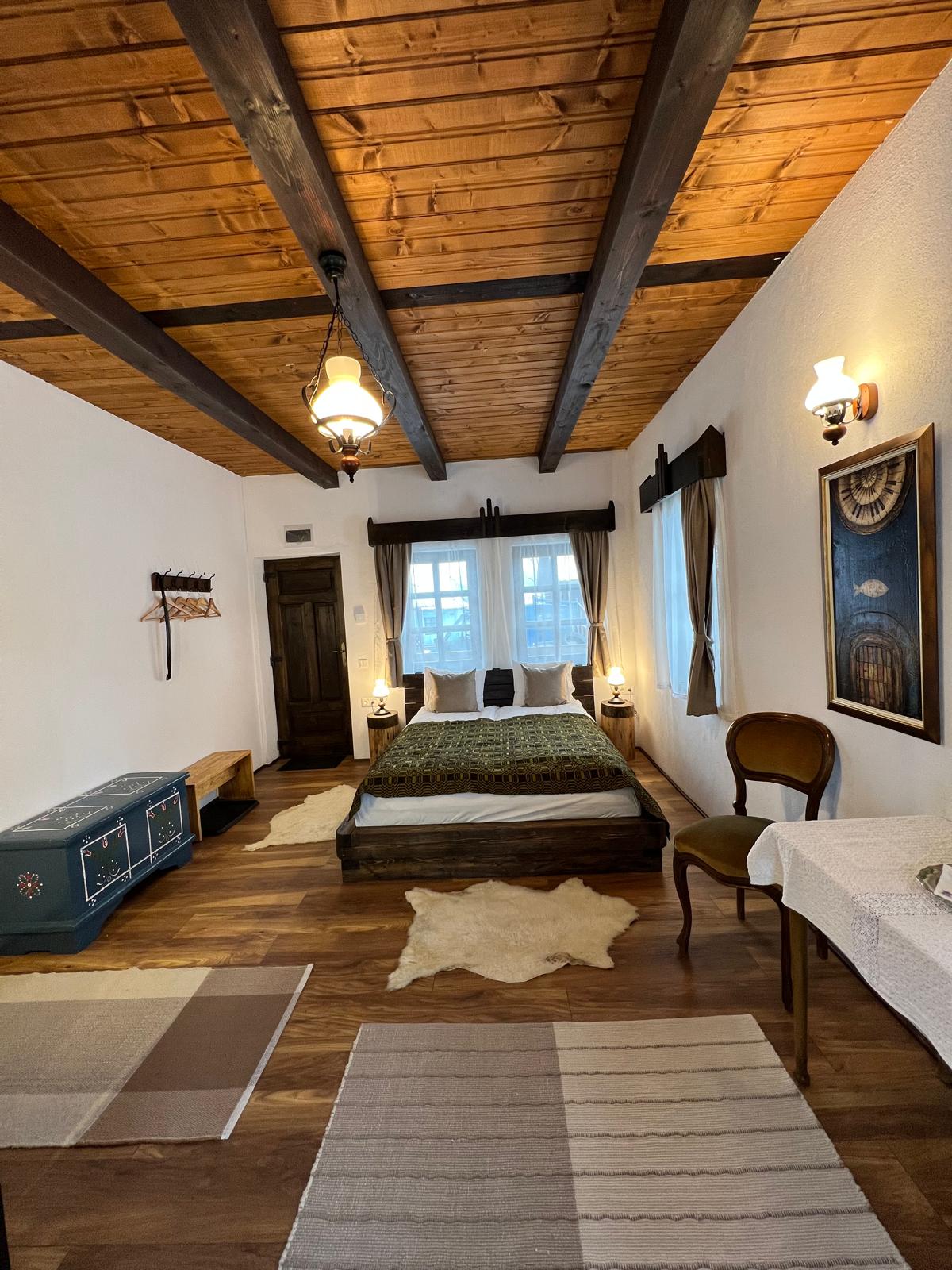 Bedroom with a dark platform bed, a sheepskin rug, a blue folk-painted chest, and an antique upholstered chair.
