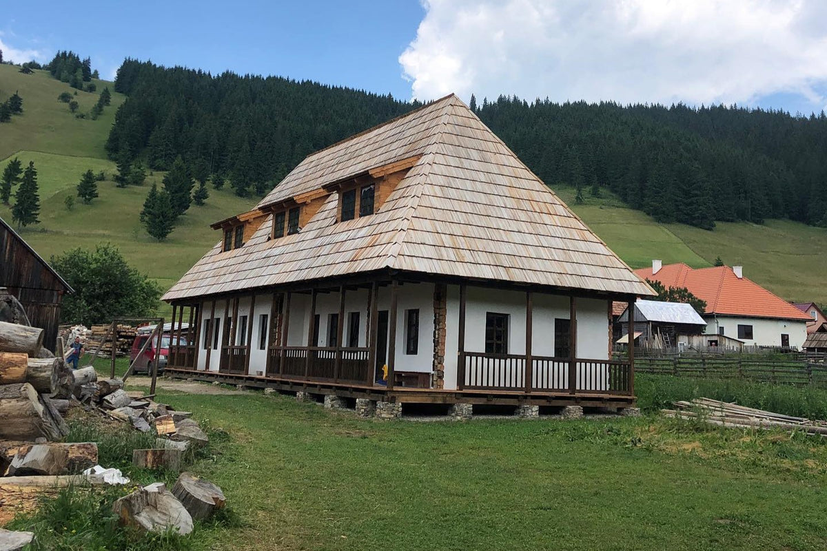 Csorja house under construction, its roof shingles still fresh and pale, with logs stacked beside it.