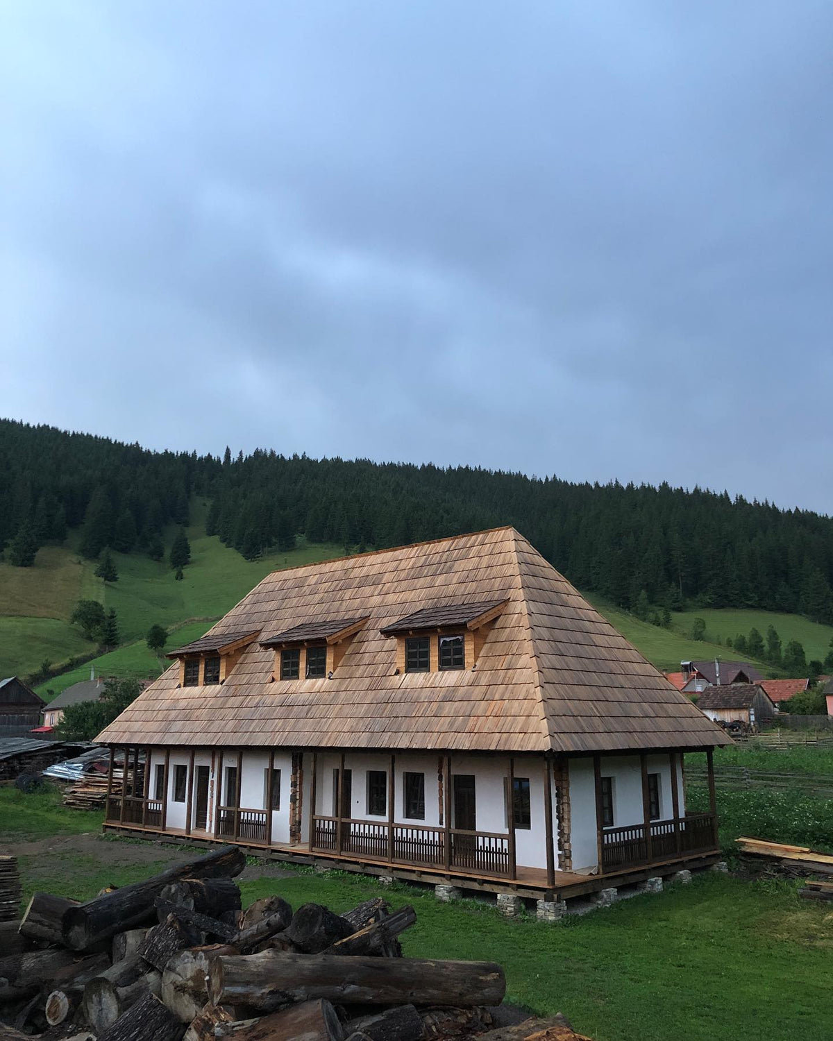 Csorja house under a dramatic stormy sky, still under construction, with cut logs piled in front.