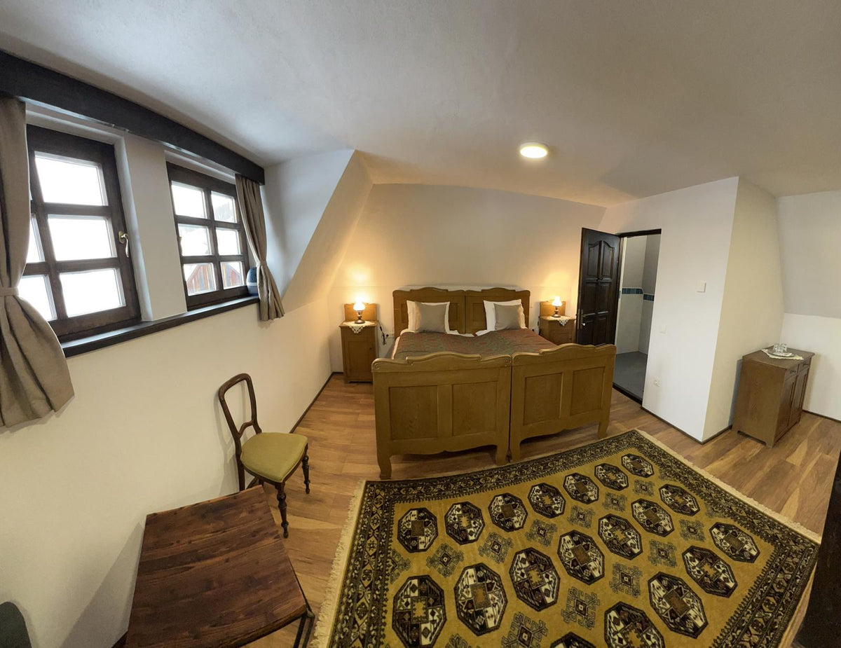 Attic bedroom with an oak wood bed, a patterned rug, and an antique chair, ensuite door open beyond.