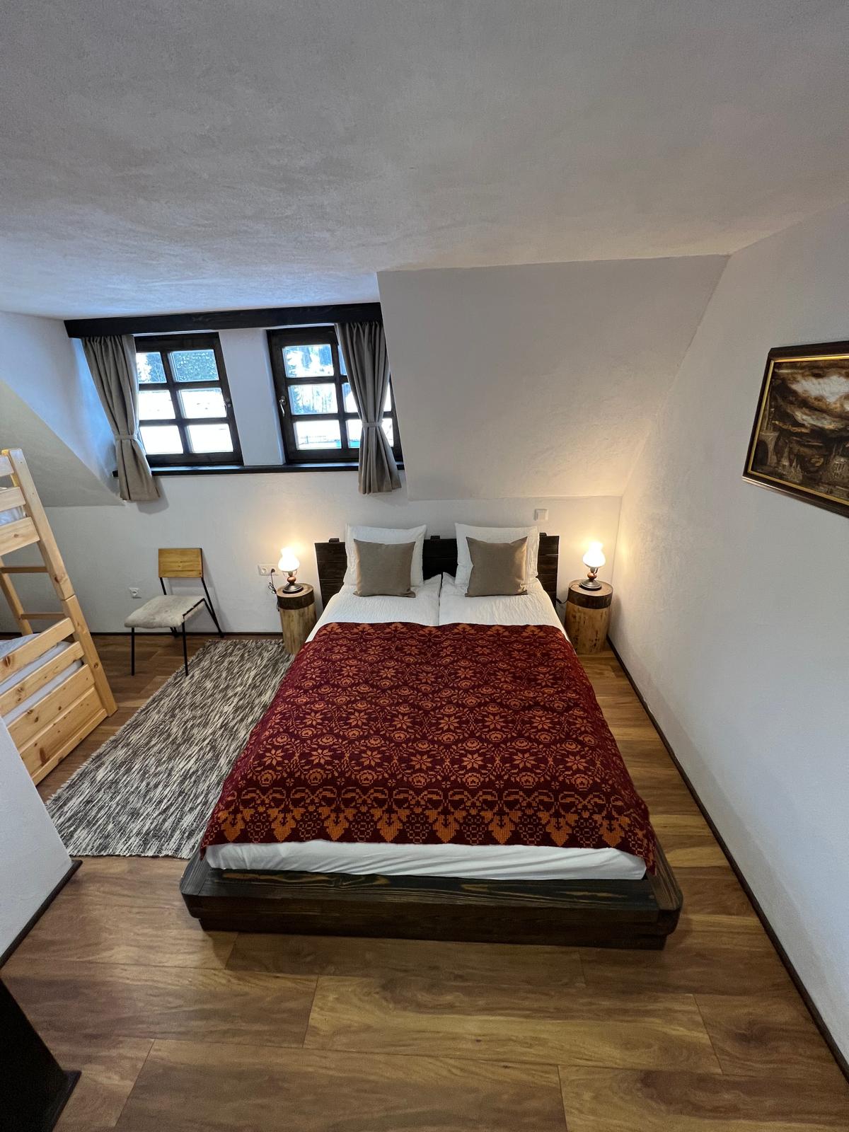 Attic bedroom with a double bed in a red and orange throw, a wood bunk bed, and a framed painting.