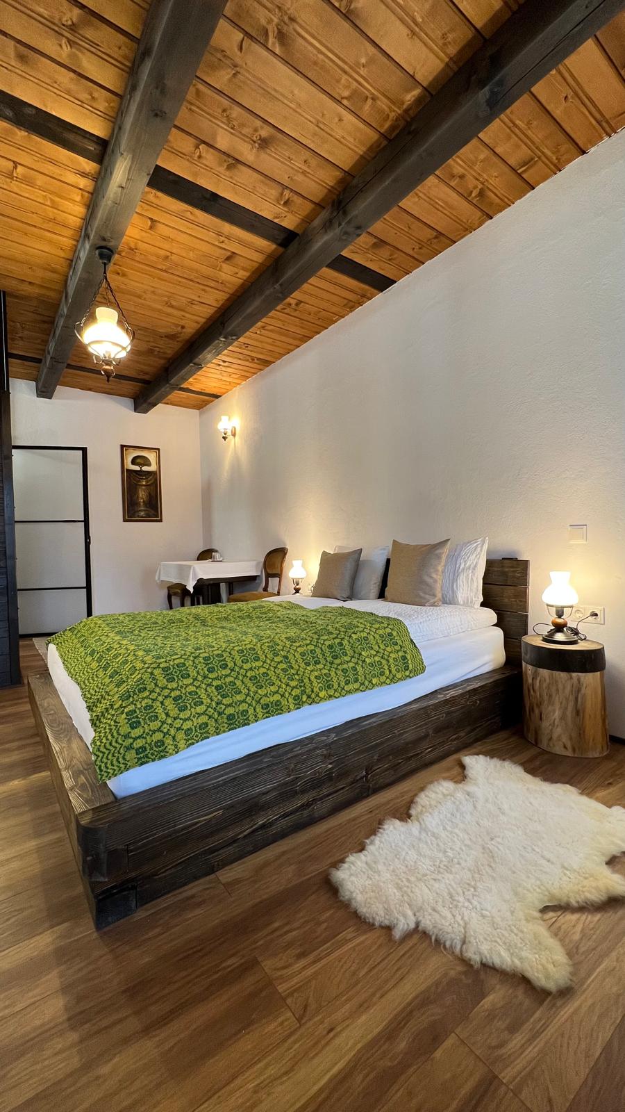 Bedroom with a low dark platform bed, a green folk-pattern throw, and a sheepskin rug on the floor.