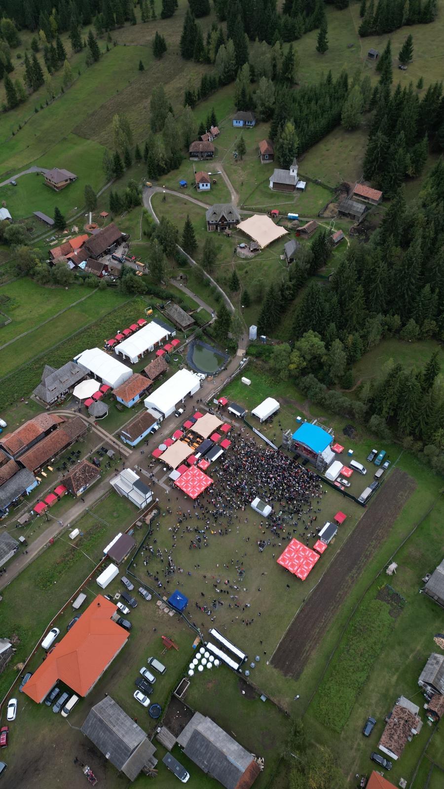 Aerial view of the Taste of Transylvania festival with crowds, stage tents, and village buildings in a mountain valley.