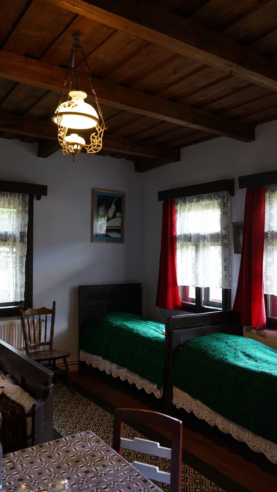 Bedroom with twin beds in lace-trimmed green bedspreads, red curtains, and a wood-beamed ceiling.