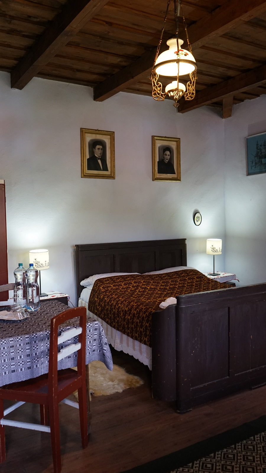 Bedroom with a dark wood-paneled bed, mustard patterned throw, and vintage portrait paintings above the headboard.