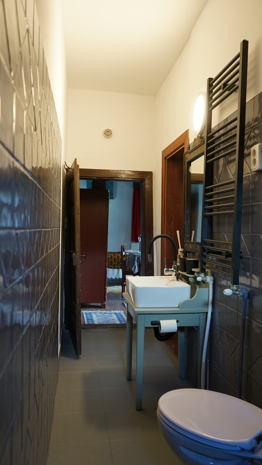 Bathroom with a vessel sink on a painted vanity stand, doorway open to a bedroom beyond.