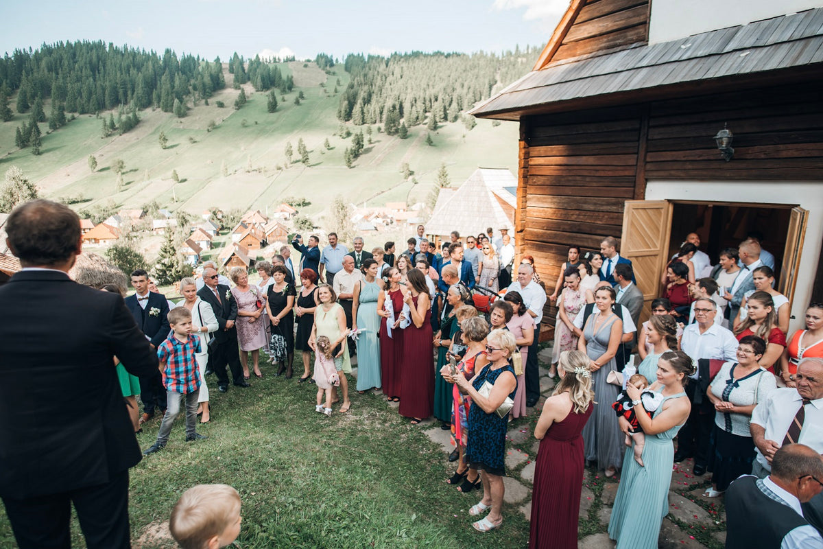 Wedding guests gathered outside the wooden chapel, hills and the village rooftops spreading below.