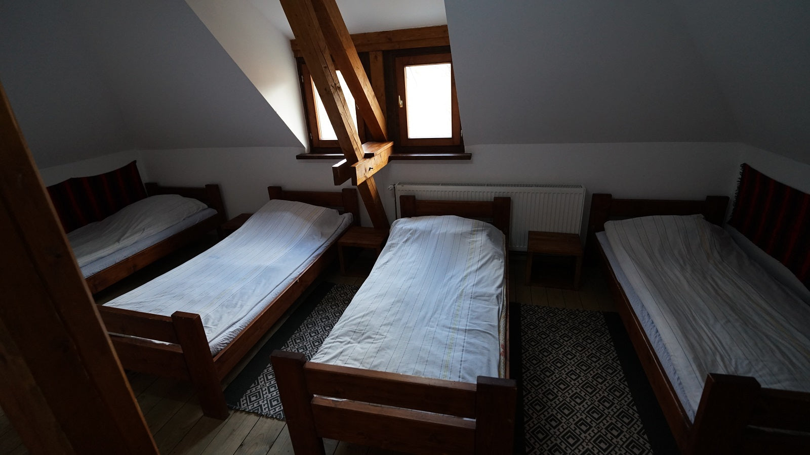 Attic dormitory room with four wooden twin beds under a sloped, exposed-beam ceiling.