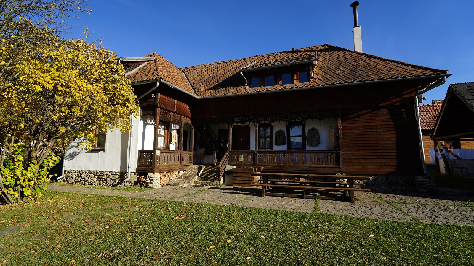 Fogadó Ház in autumn, with a golden-leaved tree in the foreground and a picnic table on the patio.