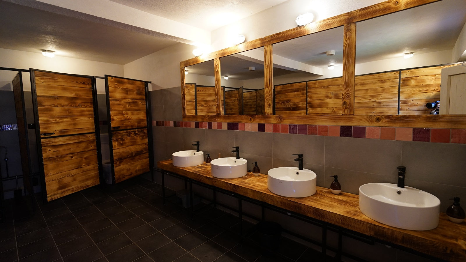 Women's washroom with a row of vessel sinks and individual soap dispensers, trimmed in red tile.