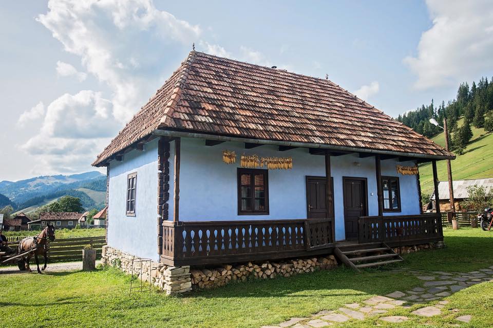 Gyimesbükki house with dried corn cobs hanging on the porch, a horse and cart passing by.