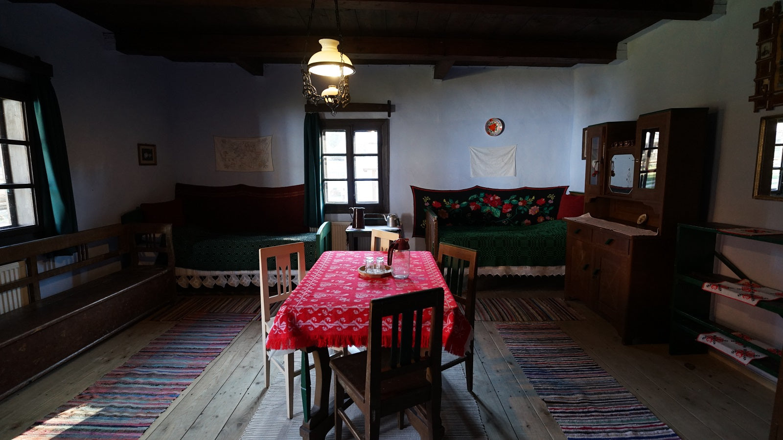 Sitting room with green upholstered benches, a rose-pattern woven blanket, and a red patterned tablecloth.