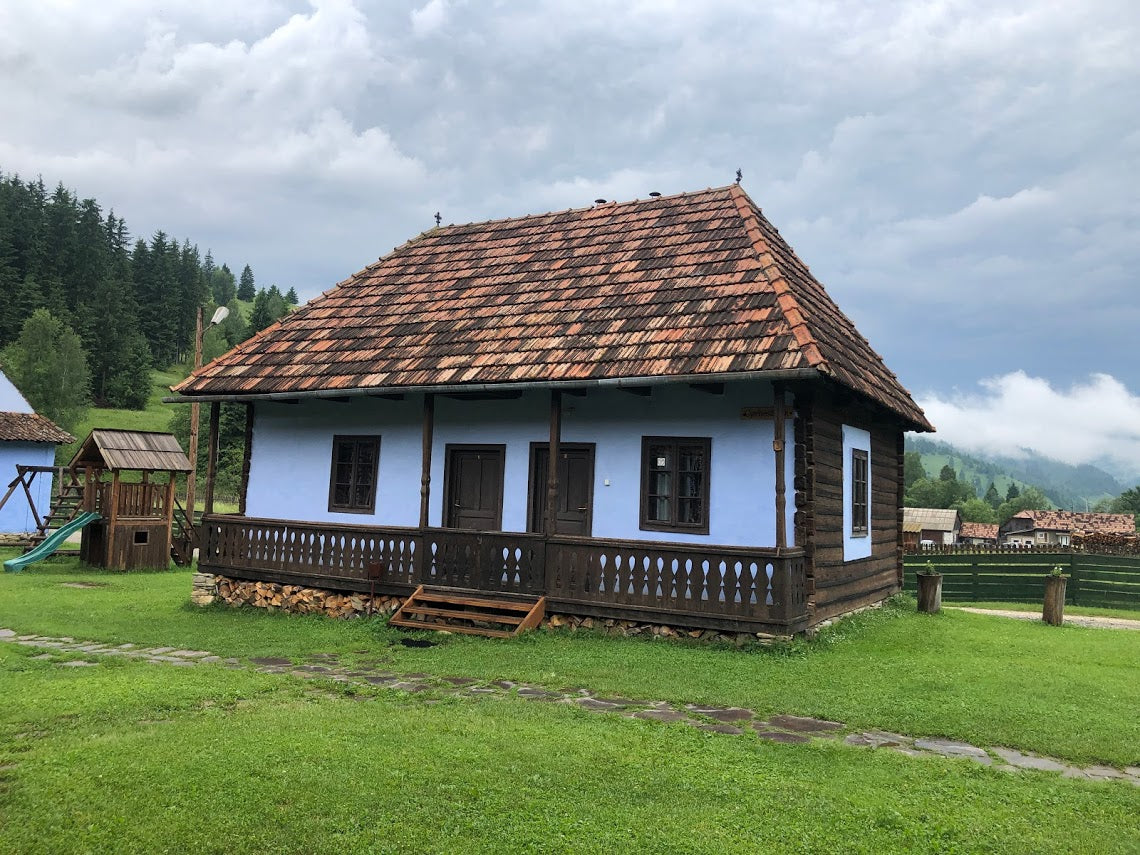 Gyimesbükki guesthouse, a pale blue house with a colorful patchwork tile roof and wraparound porch.