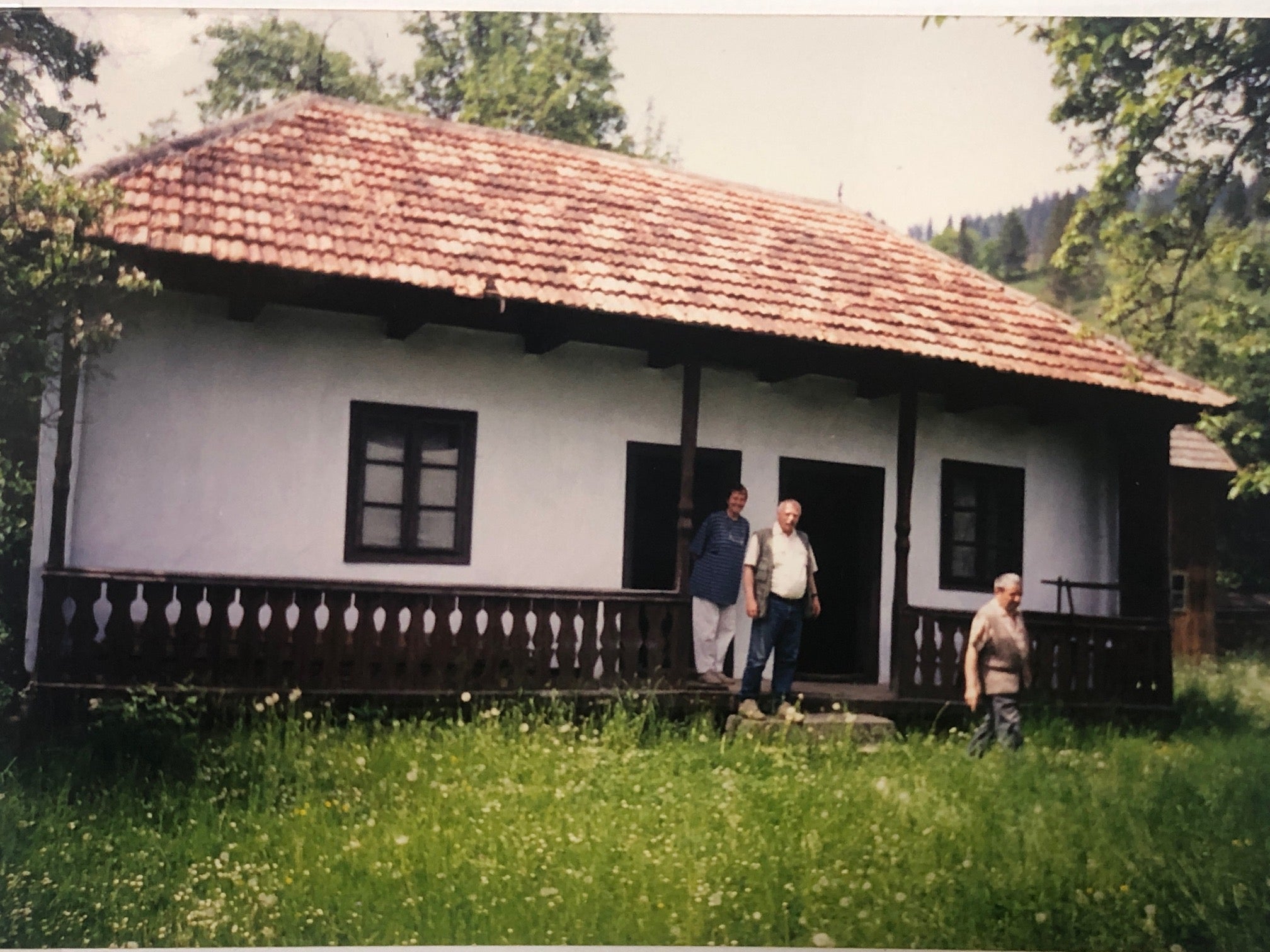 Archival photograph of the Gyimesbükki house before renovation, with three men standing on the porch.