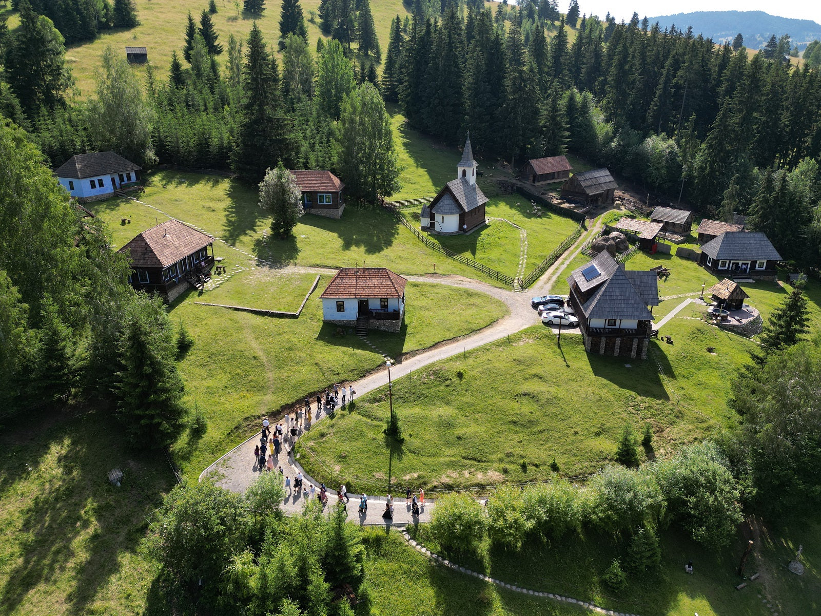 Aerial view of the finished village with visitors walking a paved path past the chapel and houses.