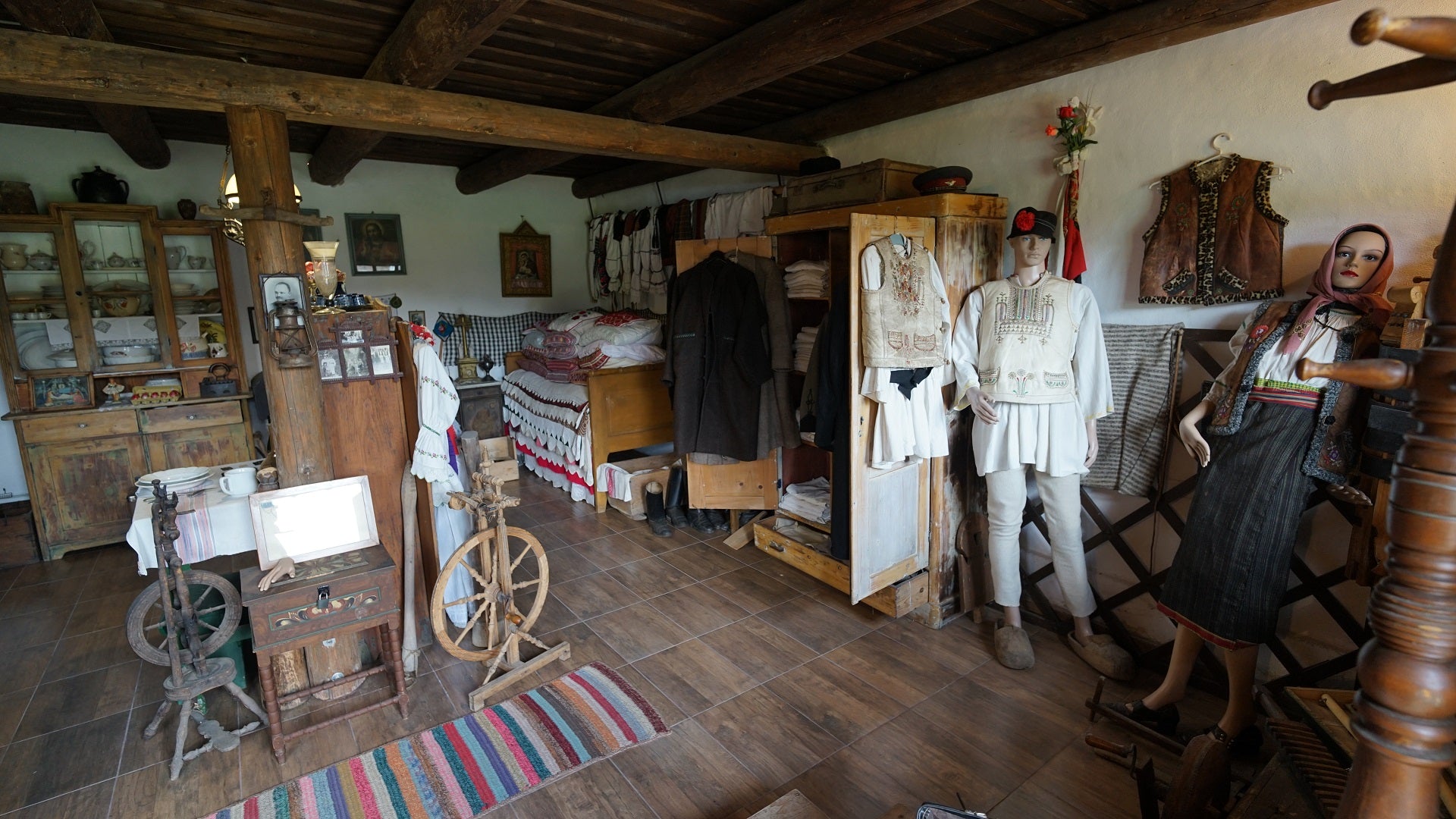 Preserved village room with two mannequins in folk costume beside an antique wardrobe and china dresser.