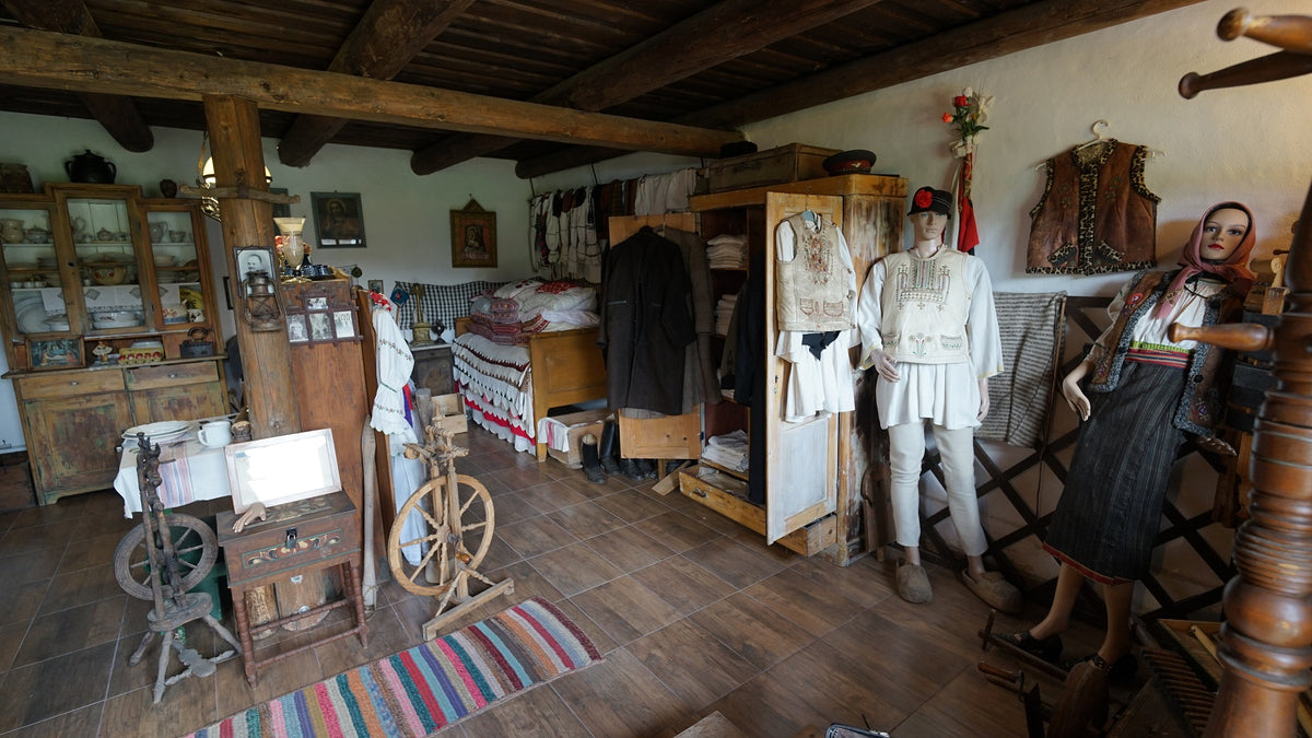 Preserved village room with two mannequins in folk costume beside an antique wardrobe and china dresser.