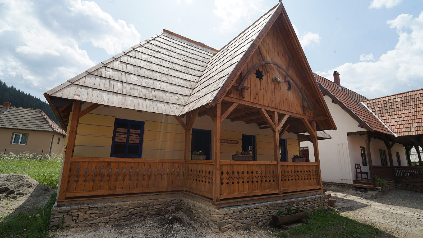 Iskola building exterior, a yellow house with a carved gable featuring a star and crescent moon motif.