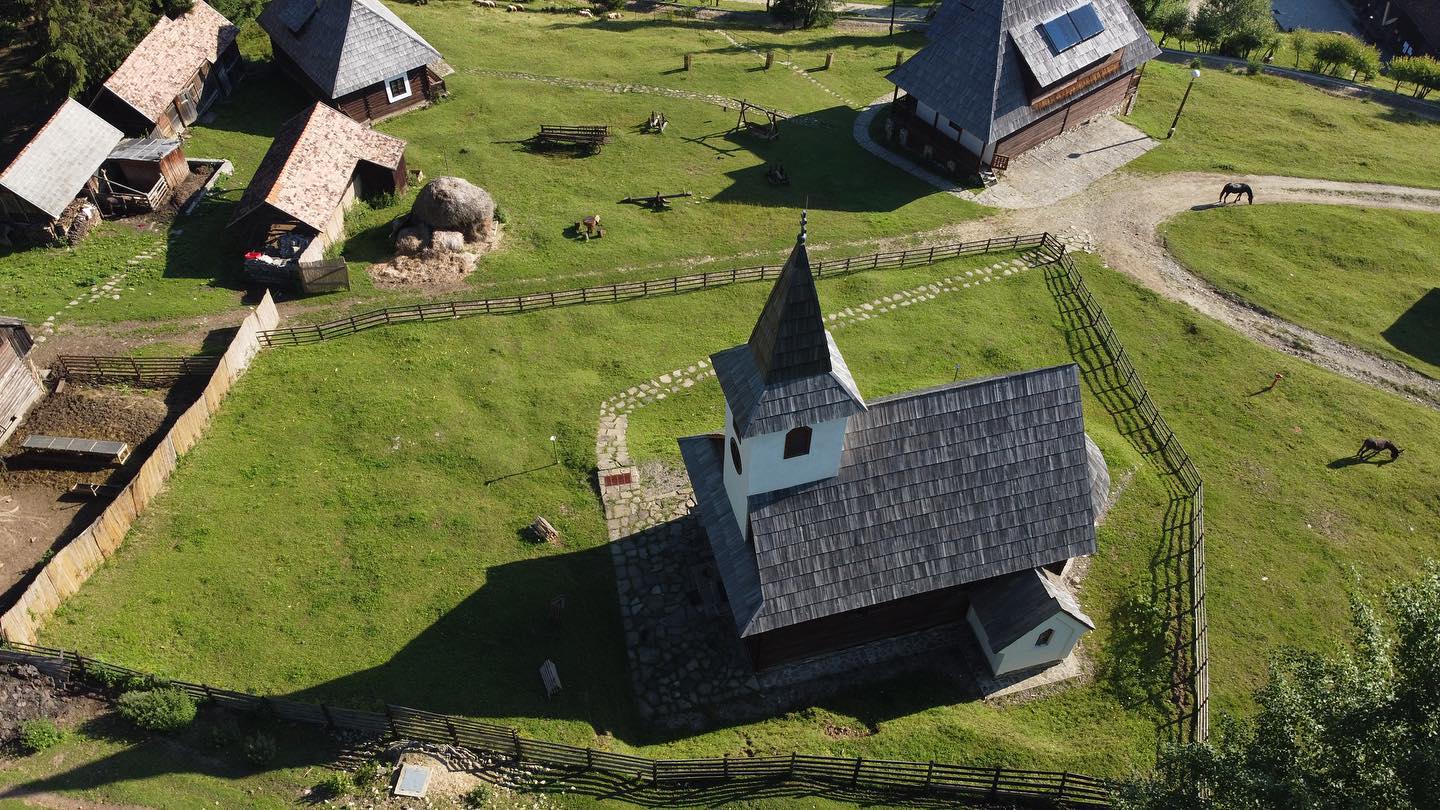 Aerial view of the chapel's steeple and shingled roof, fenced pasture and grazing horses around it.