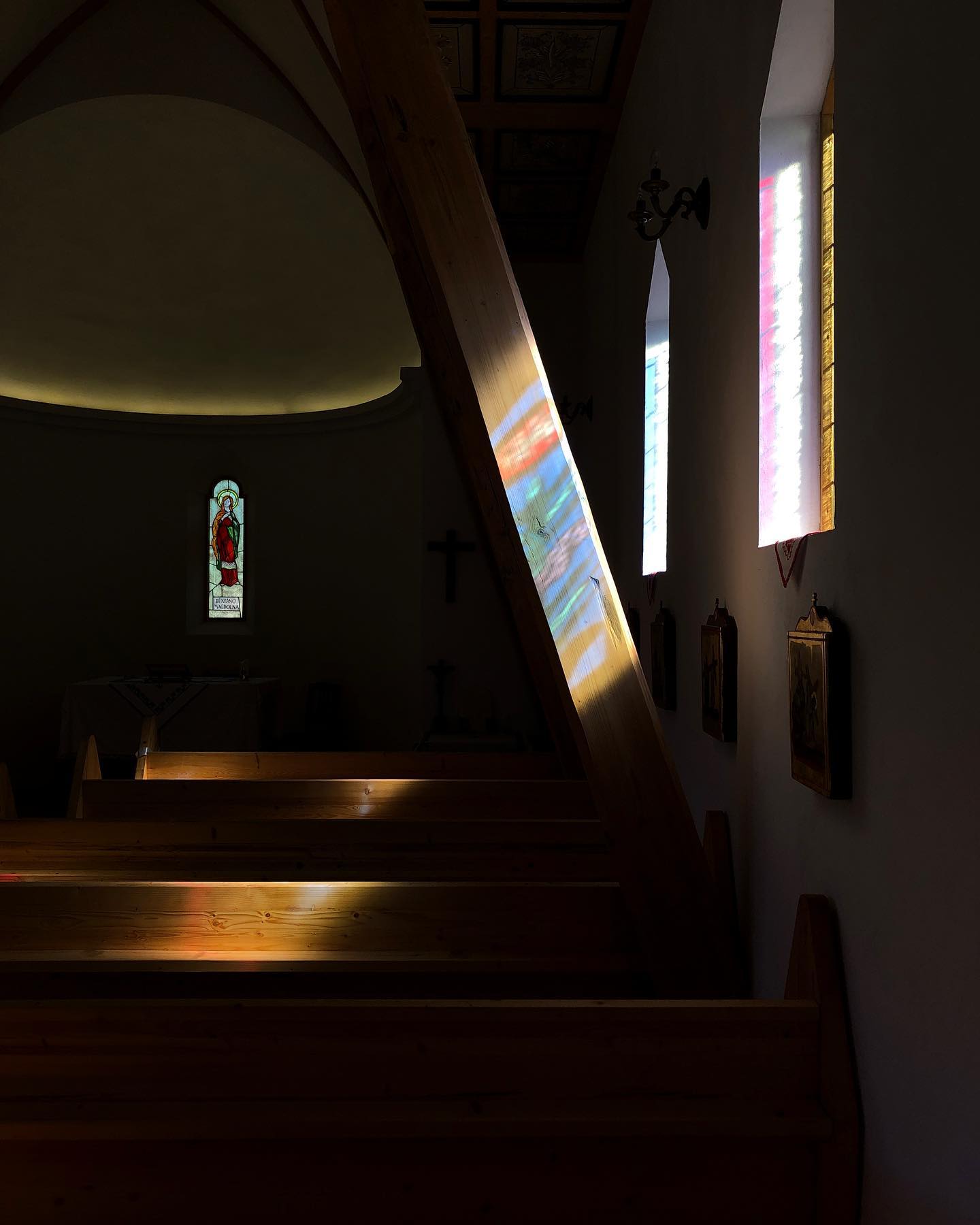Colored light streaming through stained glass windows onto the chapel's wooden pews and roof beam.