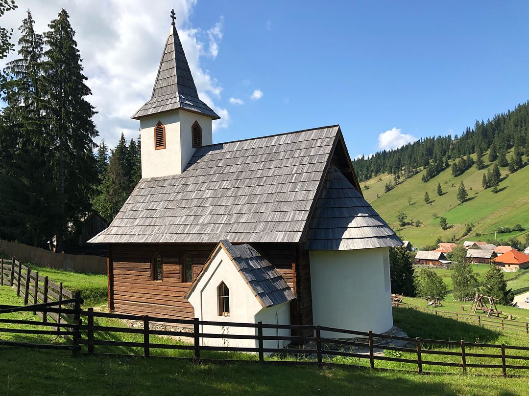 Chapel exterior with its steeple, wood-shingle roof, and stained glass windows, forested hills behind.