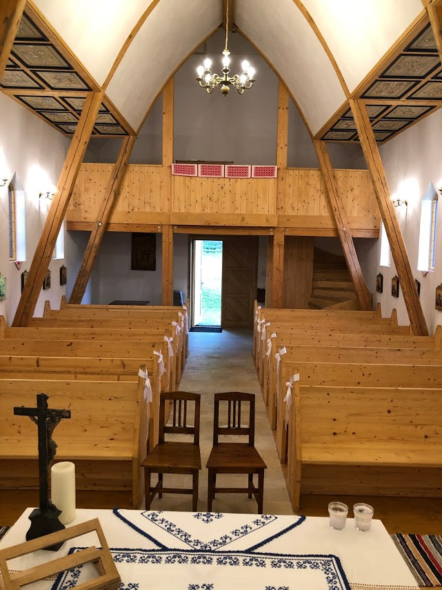 View toward the chapel entrance, with a small choir loft, wooden staircase, and white ribbons tied to the pews.