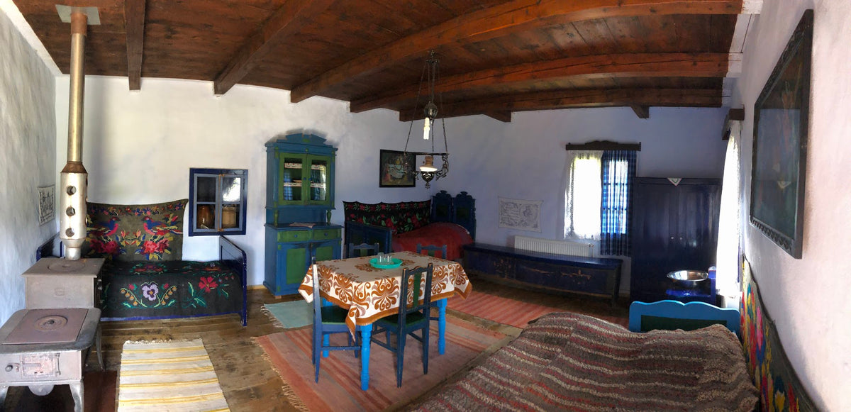 Panoramic view of a room with bird-and-floral embroidered bench covers, a blue-green cabinet, and a dining table.