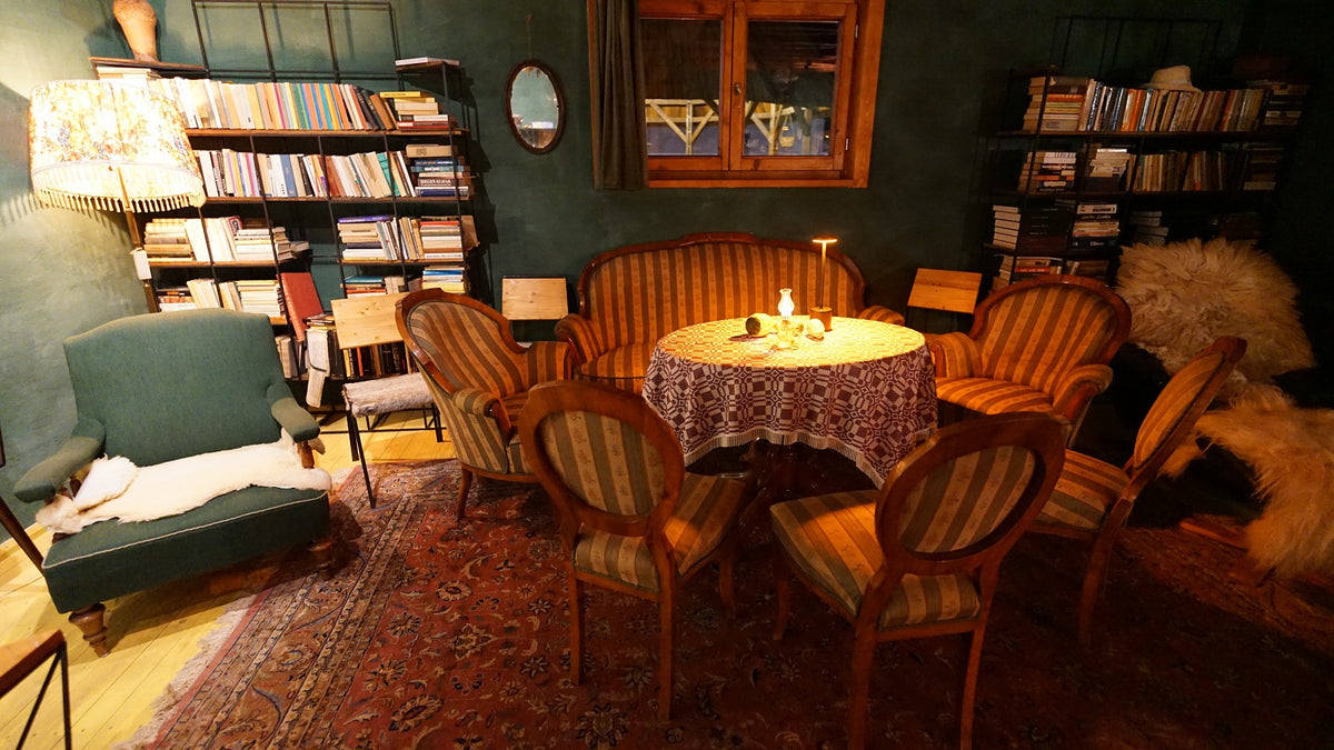 Library lounge with tall bookshelves, a round table under a checkered cloth, and a green wingback armchair.