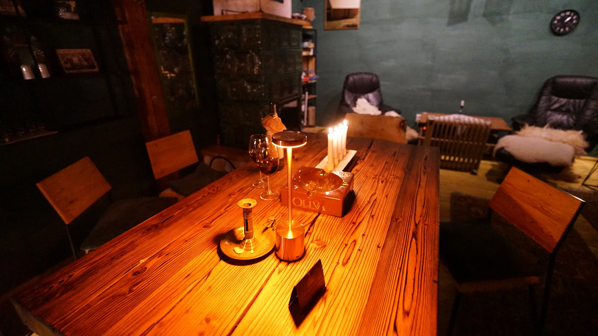 Close-up of a wooden table set with a wine glass, lit candles, and a cigar box, leather recliners behind.