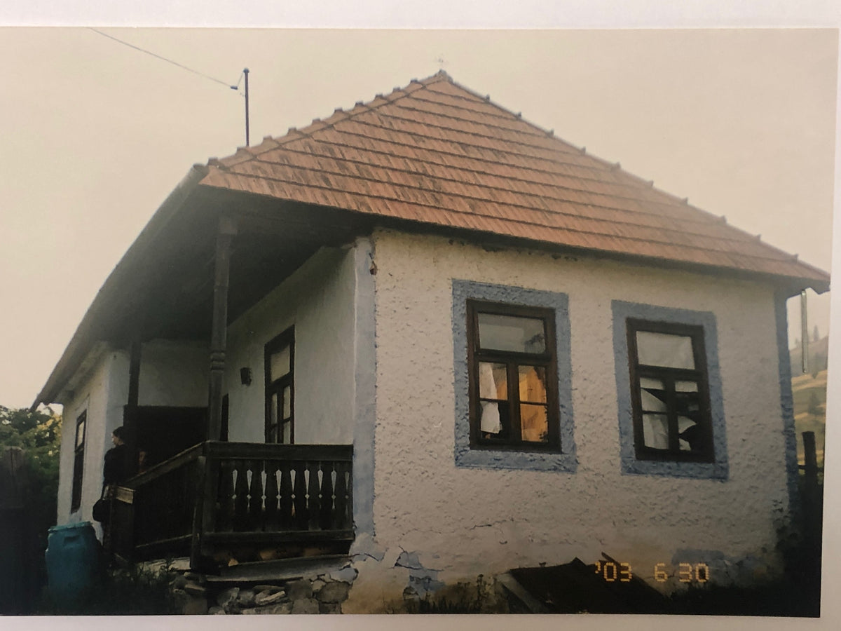 Archival photo of the Kondor house at its original site in June 2003, with a person standing on the porch steps.