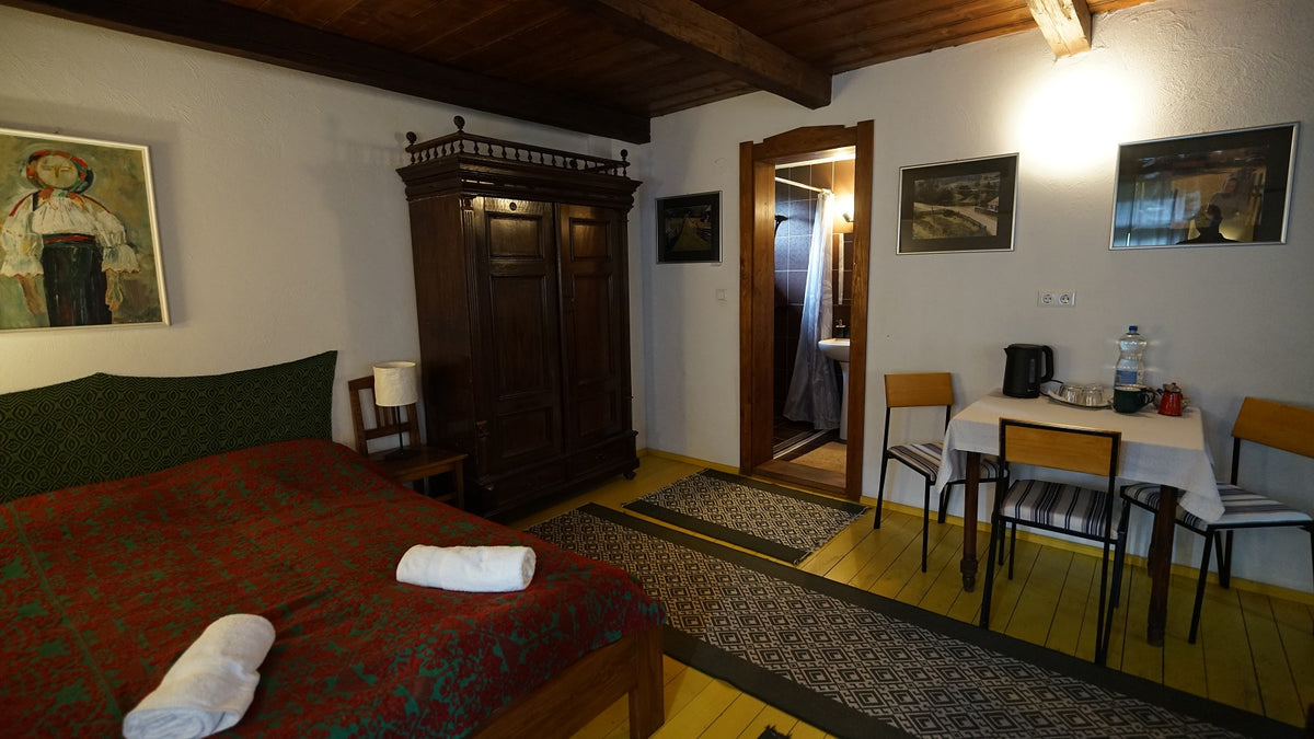 Bedroom with a red and green patterned bed, a carved antique wardrobe, and folk-art paintings on the walls.