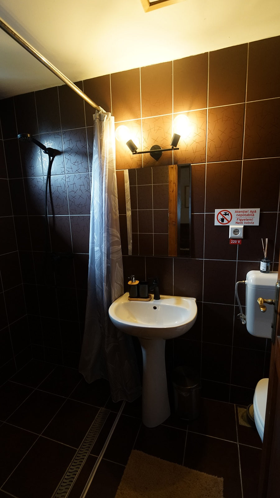 Bathroom with dark tile, a walk-in shower, and a pedestal sink.