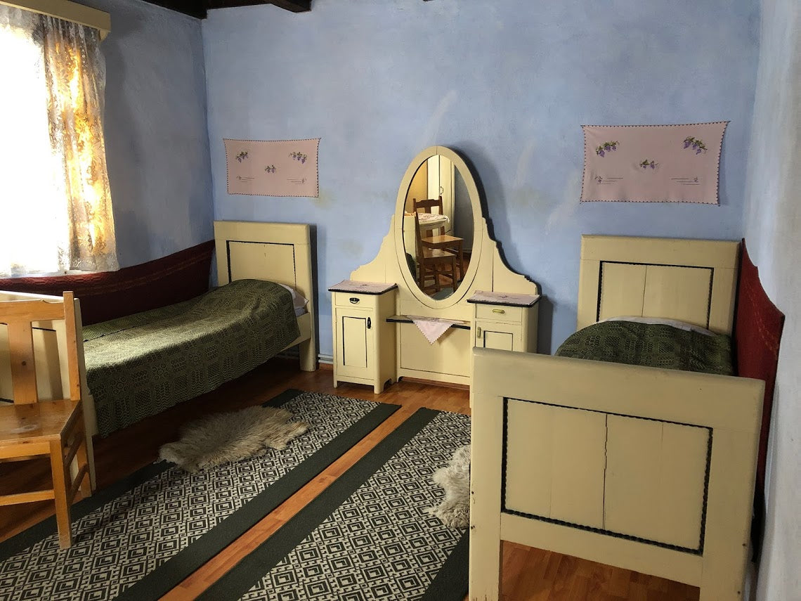 Bedroom with two cream twin beds, an oval-mirrored vanity between them, and sheepskin rugs on the floor.