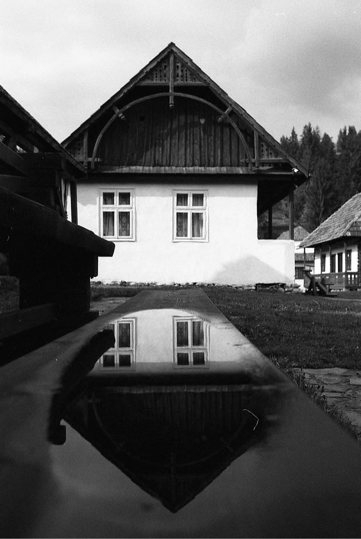 Black-and-white photo of the Madarasi house's gable end, reflected in a puddle in the foreground.