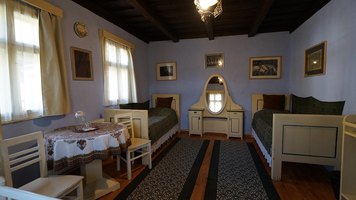 Bedroom with cream twin beds in dark green covers, an oval mirror vanity, and framed art prints on the walls.