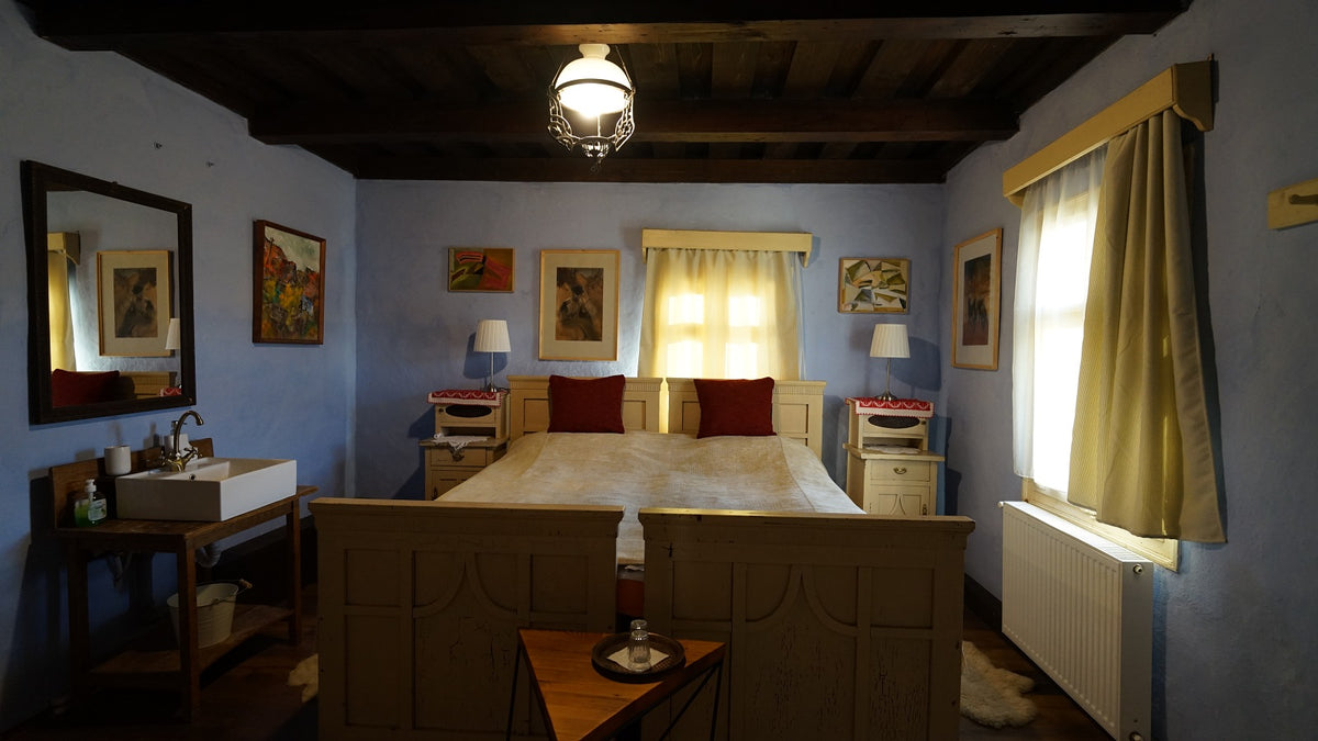 Bedroom with a carved cream wooden bed, red accent pillows, colorful modern paintings, and a corner vessel sink.